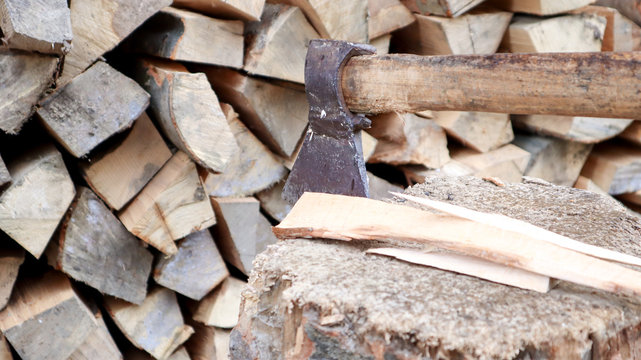 Chipped firewood for the winter for heating. The ax is stabbed with a blade into the stump. Cleaver with a wooden handle. Harvesting on the farm. Dry firewood stacked in piles for heating a house