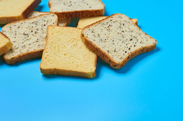 Heap of square pieces of bread with seeds and vanilla for toast lies on blue table on kitchen. Space for text