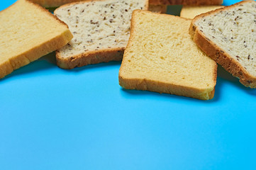 Heap of square pieces of bread with seeds and vanilla for toast lies on blue table on kitchen. Space for text