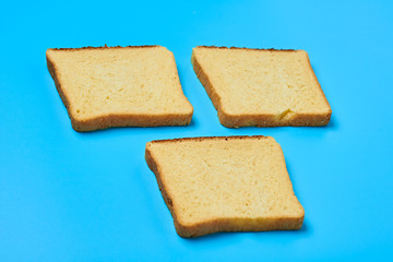 Fototapeta premium Three square pieces of yellow vanilla bread for toast lies on blue table on kitchen. Close-up