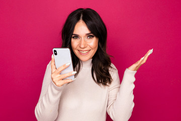 Fototapeta premium Beautiful young person standing isolated in the pink studio and holding new phone in her hands