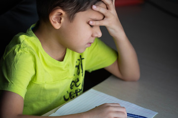 The child,  the schoolboy does not want to do difficult homework, sits at the table, bored