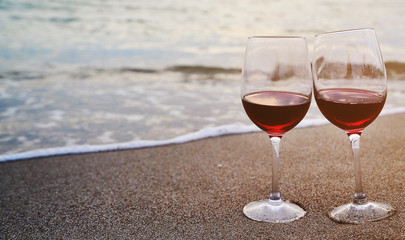 Wine glasses with red wine on sand on the beach. Valentine's Day concept.