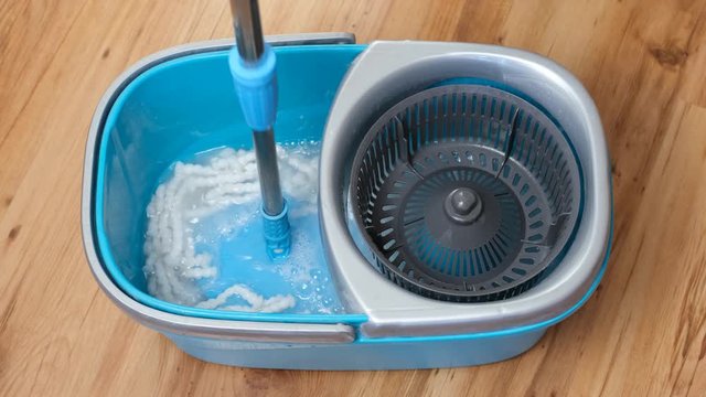 Washing and spinning the flat mop telescopic handle in a blue bucket filled with water and detergent.