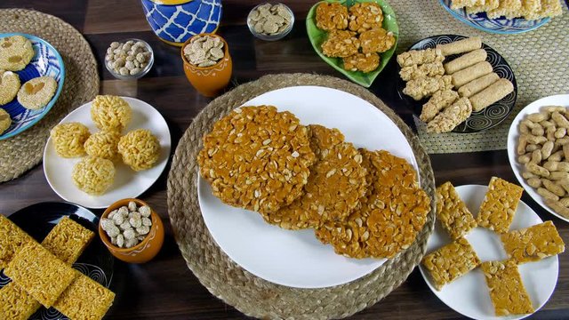 Top view shot of round peanuts chikki rotating on a turntable for Lohri celebration in India. Freshly made peanuts chikki surrounded by dry fruit gajak  bhujia chikki  rewri  murmura ladoo  gajak r...