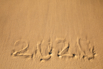 2020 summer beach holiday season written on golden sand - new season lettering on sand - numbers 2020 year  travel vacation - washed away