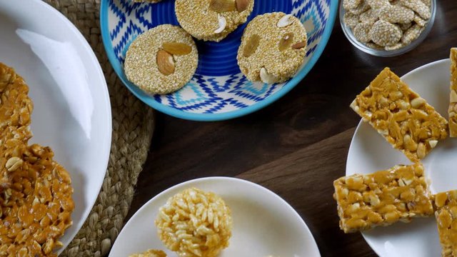 Pan shot of various Indian sweets consumed during Lohri festival - winter season. Beautifully plated murmura ladoo  bhujia chikki  peanut chikki  rewri  til chikki  groundnuts  and crispy gajaks in...