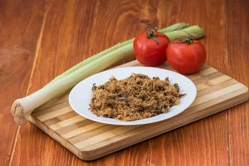 Domestic salty fried Pork greaves, duvan cvarci, in a white plate with Tomato and Leek on a Cutting Board and on Wooden Table