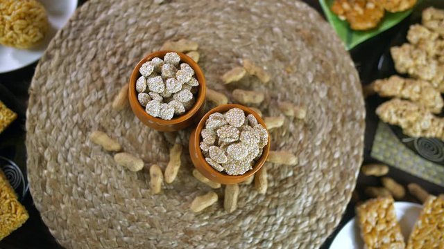 Closeup shot of homemade Indian sweet called Rewri in colored bowls - Lohri festival. Fresh rewris made with gud and a coating of sesame(til) seeds rotating on jute placemat with roasted groundnuts...