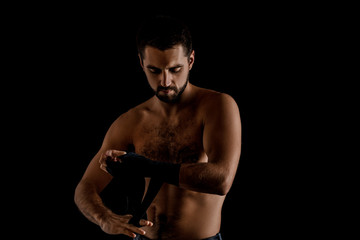 Fototapeta na wymiar Muscular man boxer wearing black strap on wrist and preparing for combat on black background