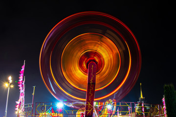 Photo of a carousel at night in a long exposure in an amusement park. The yellow and redder tones...