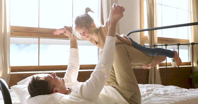 Little daughter flying as airplane playing with father in bed