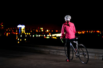 Woman Cyclist Resting with Road Bike and Looking at Night City Lights. Healthy Lifestyle and Urban Sport Concept