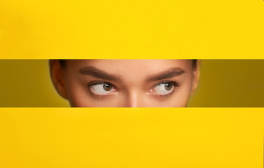 Girl's eyes peeking from hole in yellow paper, panorama