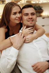 a girl in a black dress hugs the guy from behind, behind the neck and shoulders, care and love. date, valentines day