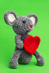 Grey knitted mouse with a heart in hand on a green background, side view