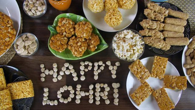 Top view shot of Lohri items beautifully plated on a wooden table for Lohri festival. Closeup shot of 'Happy Lohri' text written with rewri surrounded by peanuts chikki  gajak rolls  popcorns  bhuj...