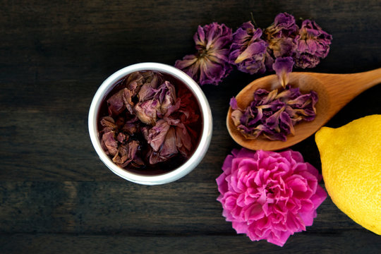 dried pink roses and tea in glass on black wood background, dry rose petala in wood spoon