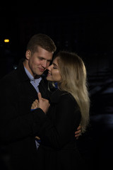 couple in love embracing against a dark background, night, rain, buildings in the city, a park, smiling, attraction. the guy hug the girl. Valentine's Day
