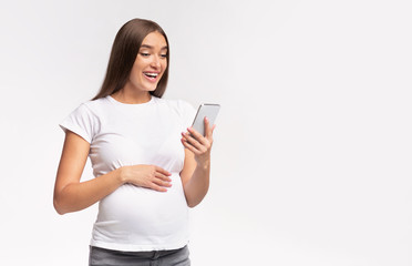 Happy pregnant woman using smartphone standing over white studio background