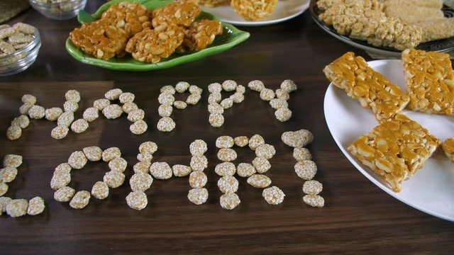 Pan shot of 'Happy Lohri' text written with rewri on the festival of Lohri in India. Closeup shot of Lohri items like peanuts chikki  gajak rolls  murmura ladoo  rewri  bhujia chikki  and groundnut...