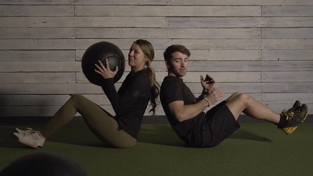 Couple passing medicine ball as they balance as part of a team workout in gym.