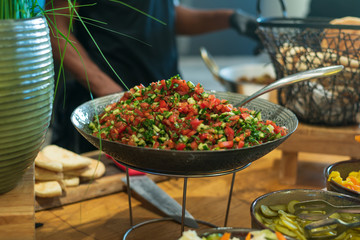 Vegetable salad with herbs in a large beautiful oriental plate on a stand with a large spoon on a wooden table. Buffet, catering. Horizontal close-up