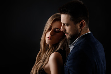 elegant couple on black background. man embracing beautiful woman in black dress. copy space