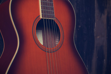 Obraz premium Cropped image of vintage style travel size acoustic guitar with rosewood neck and no pickguard on grunged dark wood textured background. Close up, copy space for text, top view.