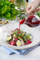 Pouring kvass, beetroot drink into a traditional Russian summer beetroot soup (okroshka) with eggs...