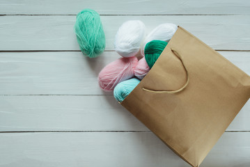 scatter oval acrylic colorful wool yarn thread skeins lying with kraft paper brown package on white...