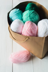 oval acrylic colorful wool yarn thread skeins lying near and into kraft paper brown package on white wooden boards background, view from angle above, vertical stock photo image