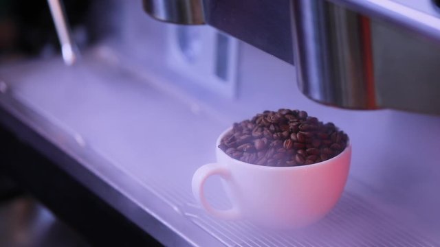 Coffee beans in the porcelain cup.  A full cup of coffee beans is shrouded in steam in a coffee machine.