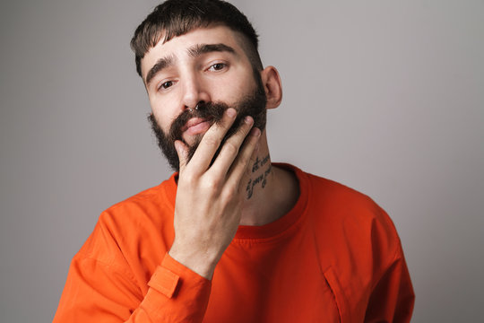 Image of young unshaven man with nose jewelry touching his beard