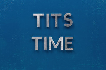 the words tits time laid with silver metal letters on classic blue board in flat lay with central...