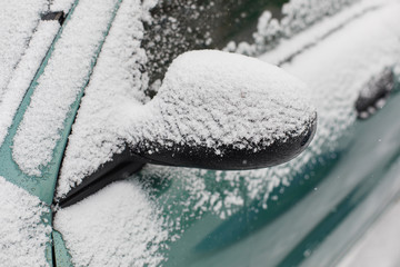 Closeup of snow covered mirror of green car