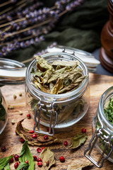 Tabletop scene of a glass cup full of dehydrated dry leaves of basil on a wooden cutting board. Vegan raw nutrition
