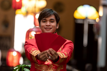 Asian man in red traditional chiness suit stand at stair,hand hold red envelop,feel happy and hope.