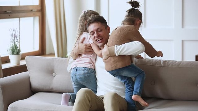 Cheerful dad hugging playing funny game with cute little daughters