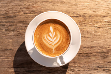 Close up a coffee latte in white cup and milk froth above to drink on brown wooden table background, increase energy for today