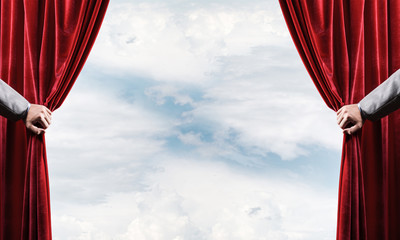 Cloudy landscape behind red curtain and hand holding it