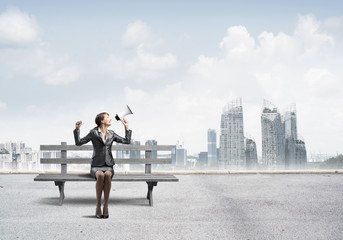 Business woman with megaphone sitting on wooden bench