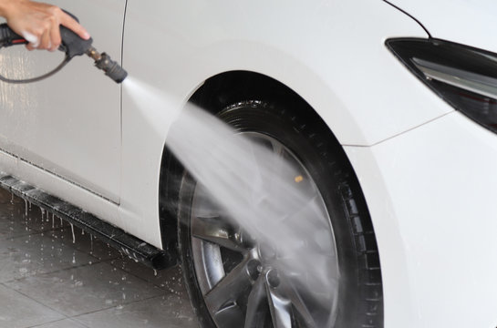 Closeup of white car cleaning, washing with  high pressure water spraying at front wheel. 