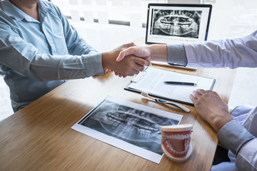 Professional Dentist showing jaw and teeth the x-ray photograph and shaking hands after finish discussing during explaining the consultation treatment issues with patient - obrazy, fototapety, plakaty