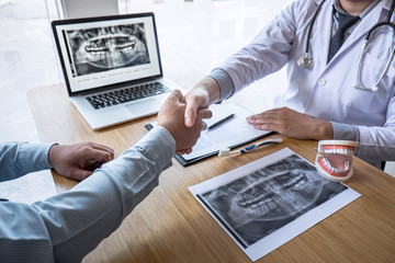 Professional Dentist showing jaw and teeth the x-ray photograph and shaking hands after finish discussing during explaining the consultation treatment issues with patient