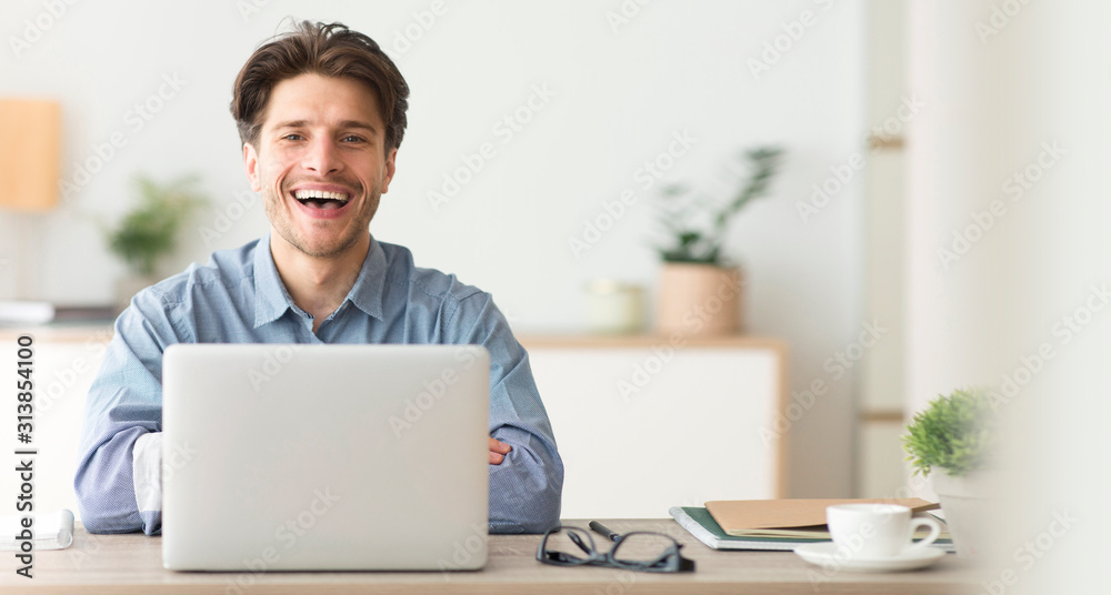 Poster happy employee smiling at camera while working on laptop in office