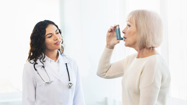 Physician examining mature woman using blue asthma inhaler