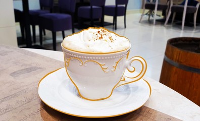 Cup with cappuccino and cream foam is on the table, framing the contour of the cup with a colored pencil