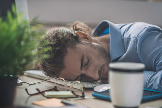 Young Bearded Man In Blue Shirt Having A Nap At Work