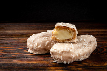 Coconut eclairs or custard cookies on dark wooden background.